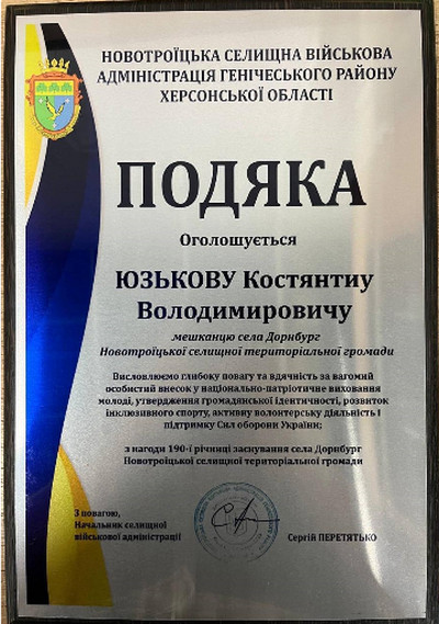 Офіційна подяка від Новотроїцької селищної військової адміністрації Костянтину Юзькову з нагоди 190-річчя села Дорнбург за патріотичне виховання молоді, розвиток спорту, волонтерство та підтримку Сил оборони України. Внизу стоїть печатка та підпис Сергія Перетятька.