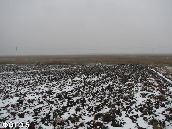 Вид на падину за селом у південному напрямку з боку клубу та школи: відкритий пейзаж із зораним полем, притрушеним першим снігом, під похмурим зимовим небом. 