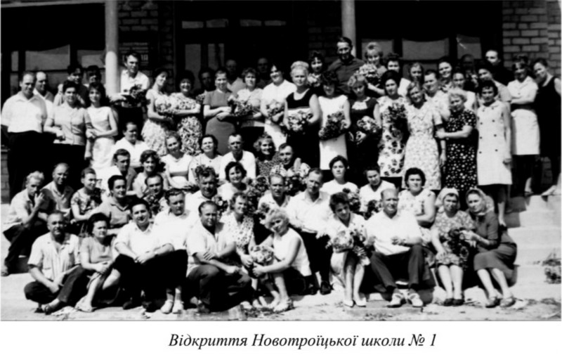 Архівне чорно-біле групове фото вчительського та шкільного колективу на сходах перед будівлею школи на честь її відкриття, багато з яких тримають у руках букети квітів. Підпис під фото: «Відкриття Новотроїцької школи № 1