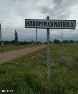 Дорожній вказівник із назвою села «Новомихайлівка» на тлі сільської дороги та неба